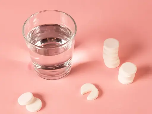 Ein Glas Wasser und Magnesium-Brausetabletten auf rosa Untergrund. Hilft Magnesium beim Einschlafen?