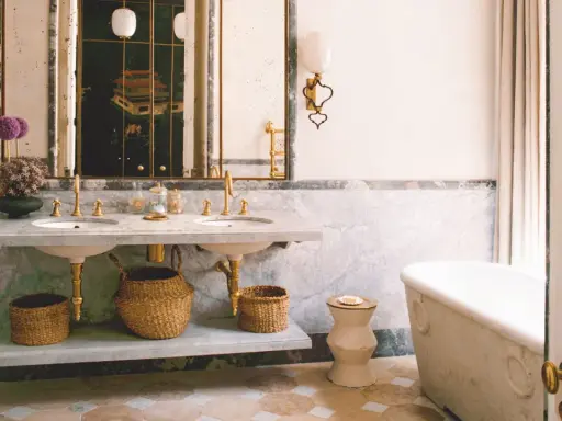Elegante baño con doble lavabo de mármol, bañera exenta y suelo de baldosas. Un espejo con marco dorado y un cuadro oriental añaden un toque de lujo. ¡Ideas para pintar azulejos baño!