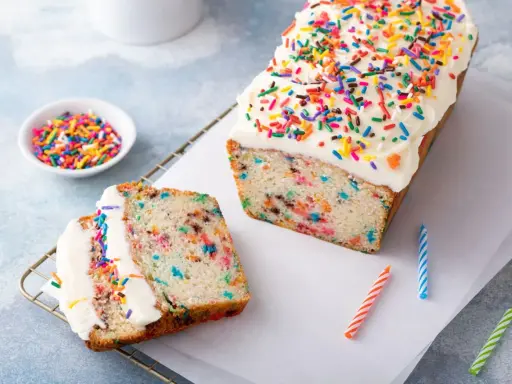 Bunter Konfetti Kuchen mit weißer Glasur und Streuseln. Ein Stück ist angeschnitten und zeigt die bunten Sprenkel im Teig.