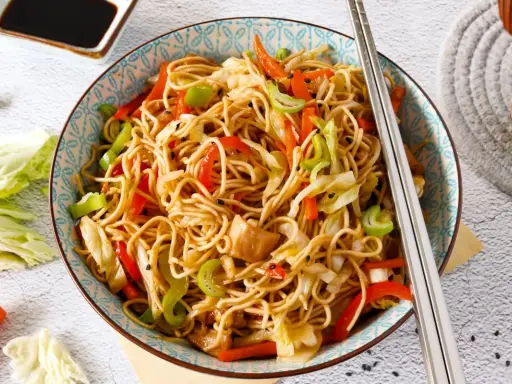 Un plato de chow mein con verduras coloridas y palillos listos para disfrutar.