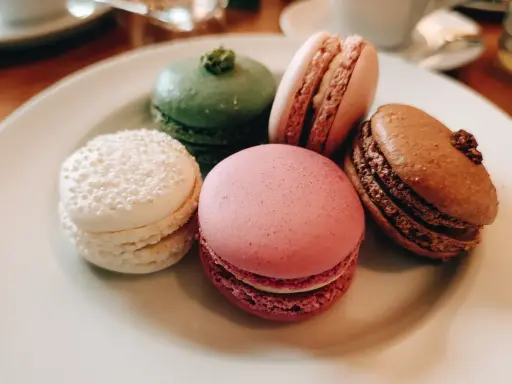 Fem färgglada macarons på en tallrik. En vit med pärlor, en grön, en rosa, en ljusrosa och en brun. Perfekt för ett macarons recept.