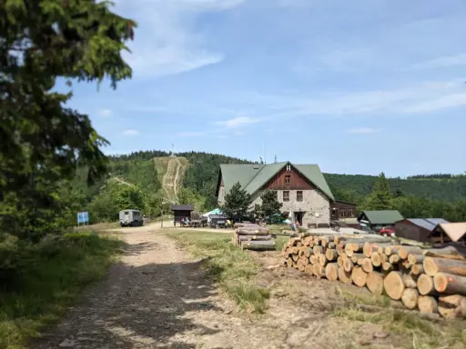 Kamienna chata i stosy drewna przy szlaku na Klimczok. W tle widać górę z wytyczonymi ścieżkami i las.