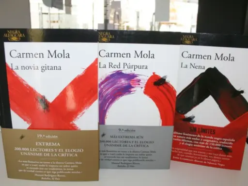 Libri di Carmen Mola: "La novia gitana", "La Red Púrpura" e "La Nena". Copertine con disegni astratti e mosche.
