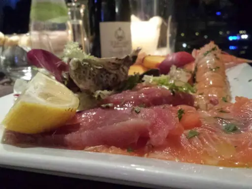 Un piatto di pesce crudo, con salmone, tonno e scampi, accompagnato da limone e insalata. Un'ottima occasione per degustazioni gastronomiche.