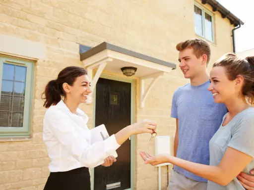 Une agent immobilier remet les clés d'une maison à un jeune couple. Ils sont heureux d'acquérir leur nouveau logement, peut-être grâce au droit de préemption locataire.