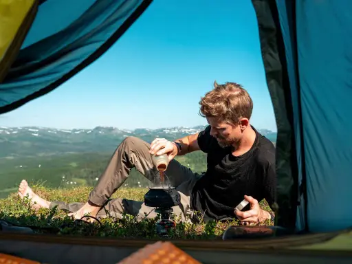 Man förbereder kaffe utanför tältet med en fantastisk utsikt. En del av packlista vandring sommar.