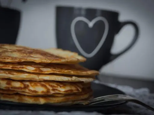 Stapel goldbrauner, **high protein pancakes** auf schwarzem Teller, daneben eine Tasse mit Herz.