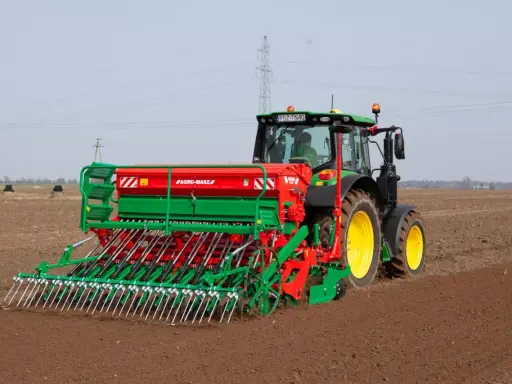 Zielony traktor z siewnikiem Agro-Masz pracuje na polu. Maszyna precyzyjnie wysiewa nasiona, optymalizując ile trawy na hektar zostanie zasiane.