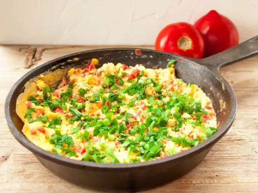 Pyszny omlet z warzywami, posypany szczypiorkiem, gotowy do podania. Obok leżą dwa pomidory.