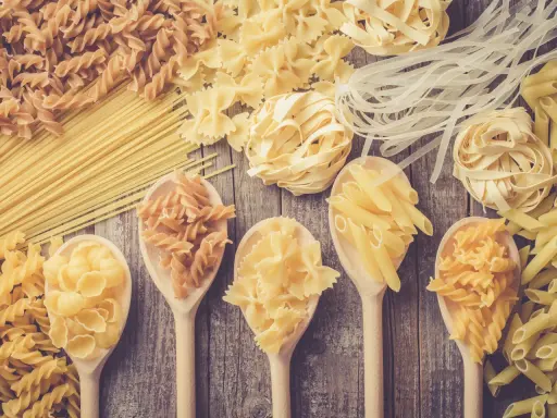 Verschiedene Nudelsorten auf Holzlöffeln und Holzuntergrund. Welche Pasta hat am wenigsten Kalorien? Vielleicht die dünnen Reisnudeln?