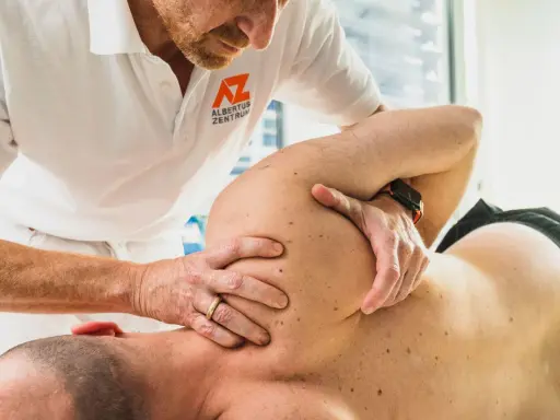 Therapeut führt eine gezielte Massage bei Schulterschmerzen durch. Hände des Therapeuten bearbeiten den Schulterbereich eines liegenden Patienten.