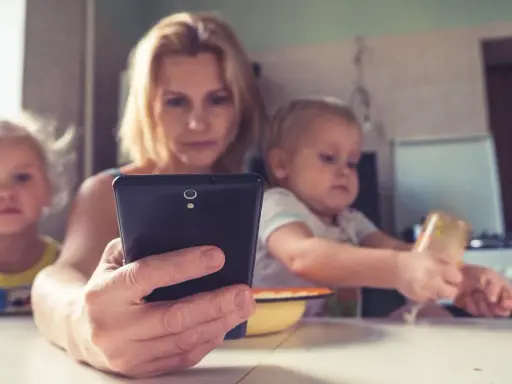 Madre con su móvil, mientras sus hijos pequeños, de unos 2 años, miran pantallas.