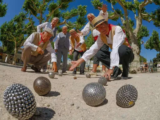 Des hommes jouent à la pétanque sous les platanes. La question "la pétanque est-il un sport ?" se pose devant leur concentration.