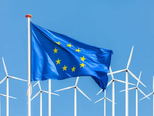 Europäische Flagge weht vor einer Reihe von Windrädern, die für erneuerbare Energien in der EU stehen.