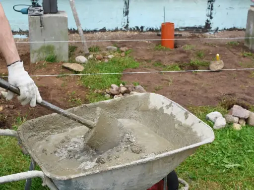Mano enguantada mezcla cemento y arena en carretilla. Preparando material para construcción.