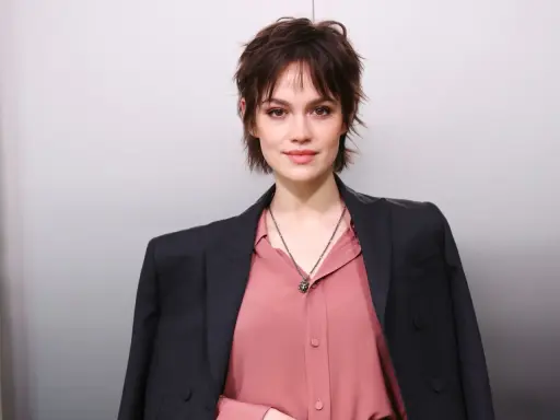 Junge Frau mit modischer Kurzhaarfrisur, inspiriert von Frisuren ab 50. Sie trägt einen rosafarbenen Blusen- und dunklen Blazer-Look.