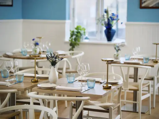 Vackert dukade bord med blåa glas och blommor i vaser, redo för gäster på en av restaurangerna i Skagen.