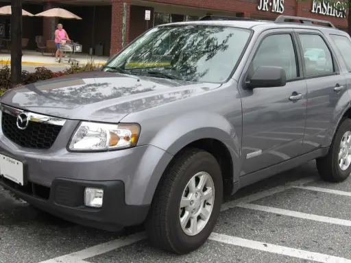 Szary Mazda Tribute zaparkowany na parkingu przed sklepem.