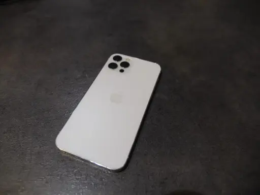 Elegancki, biały iPhone 12 Pro Max z charakterystycznym modułem aparatów na ciemnym tle.