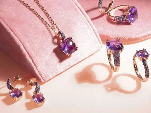 Gioielli con pietre viola intenso, un magnifico **ametista colore** che brilla su anelli, orecchini e una collana, su un morbido sfondo rosa.