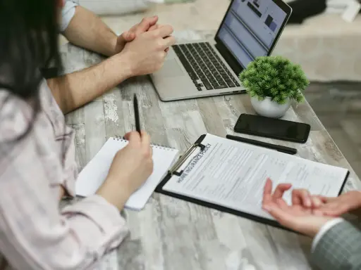Réunion pour une contre-expertise assurance : un contrat est sur la table, un ordinateur portable ouvert, et des mains discutent des détails.