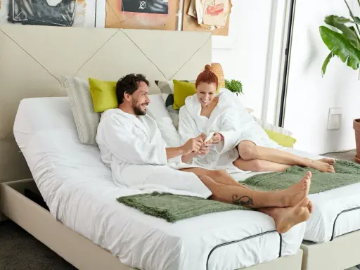 Pareja en bata blanca sobre cama articulada, aprendiendo como vestir una cama articulada para mayor comodidad.