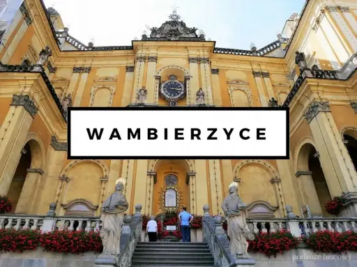 Bazylika w Wambierzycach, znana z licznych atrakcji, zachwyca architekturą. Widać schody prowadzące do sanktuarium, ozdobione czerwonymi kwiatami.