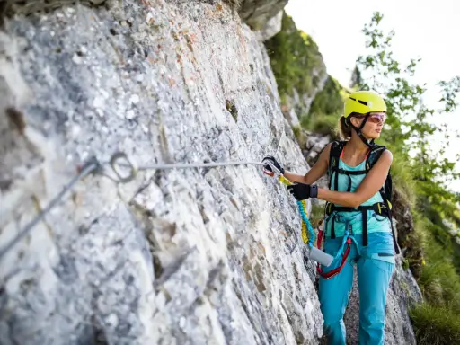 Kobieta w kasku i sprzęcie wspinaczkowym pokonuje via ferrata polska. Wspinaczka po skalnej ścianie z liną asekuracyjną.
