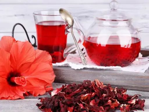 Orzeźwiająca herbatka z hibiskusa, podana w szklanym dzbanku i kubku, obok świeżego kwiatu i suszonych płatków.