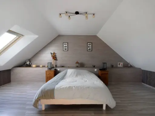 Chambre sous comble avec lit douillet, velux et décoration murale en bois.