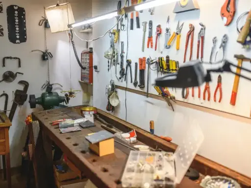 Warsztat domowy pełen narzędzi i pomysłów na majsterkowanie. Widać tu imadło, szlifierkę, mnóstwo kluczy, śrubokrętów i innych przyrządów.