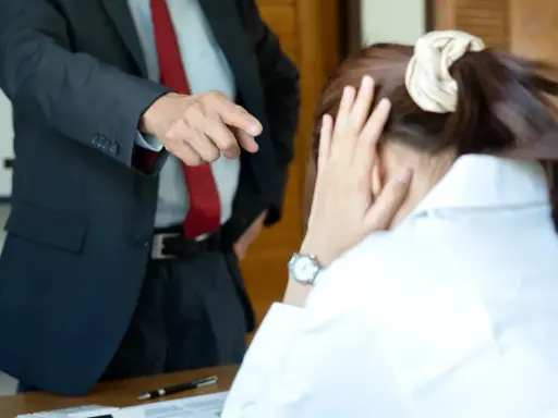 Szef wskazuje palcem na pracownika, który ukrywa twarz w dłoniach. Widać tu negatywne cechy pracownika, takie jak brak pewności siebie i stres.