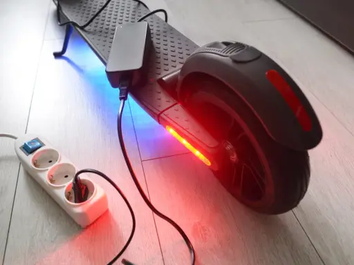 Un chargeur pour trottinette électrique est branché sur une multiprise. La trottinette est éclairée par des LED bleues et rouges.