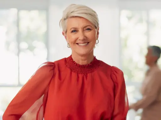 Uśmiechnięta kobieta z krótkimi blond włosami, w czerwonej bluzce. Idealna inspiracja na eleganckie fryzury na wesele dla mamy.