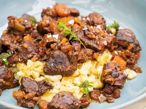 Herzhaftes Wildschwein Gulasch Rezept mit Spätzle, garniert mit frischen Kräutern und grobem Salz. Ein Genuss für Feinschmecker!