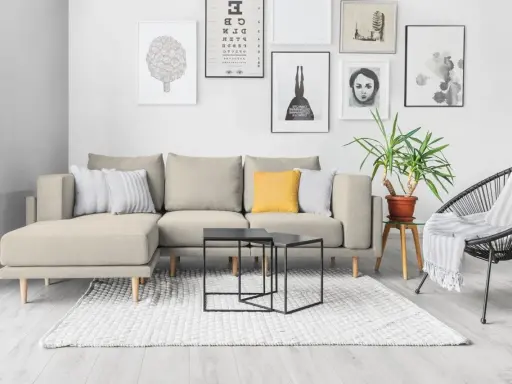 Divano componibile beige con cuscini, tavolini neri, tappeto bianco e sedia nera. Ispirazione per come foderare un divano fai da te.