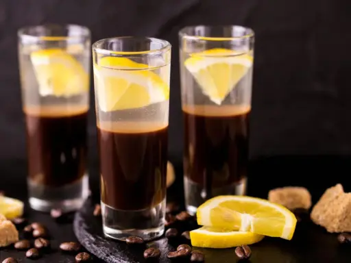 Drei Gläser mit Espresso und Zitrone, ein italienischer Genuss. Kaffeebohnen und Zuckerwürfel liegen daneben.