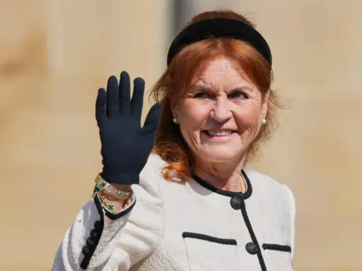 Sarah, hertiginna av York, vinkar glatt med en svart handske på sig. Hon bär en elegant ljus jacka med svarta detaljer och smycken.