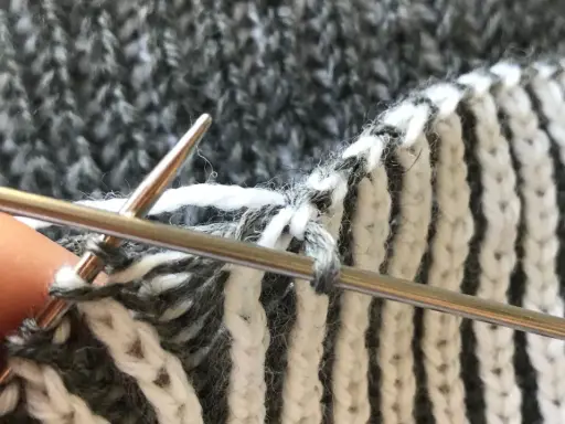 Närbild på patentstickning på rundsticka med grått och vitt garn. En tumme håller i stickan.