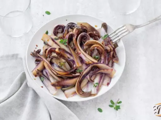 Radicchio in padella, caramellato e profumato, servito su un piatto bianco con un tocco di erbe aromatiche.