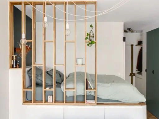Aménagement astucieux d'un studio T2 avec un lit douillet séparé par une étagère en bois.