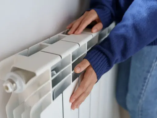 Manos frías tocan un radiador blanco que no calienta.