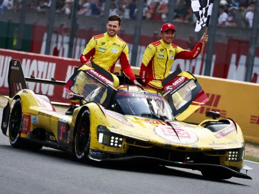 Zwei Rennfahrer in gelb-roten Overalls jubeln neben ihrem gelben Ferrari Le Mans Prototyp mit der Startnummer 83.