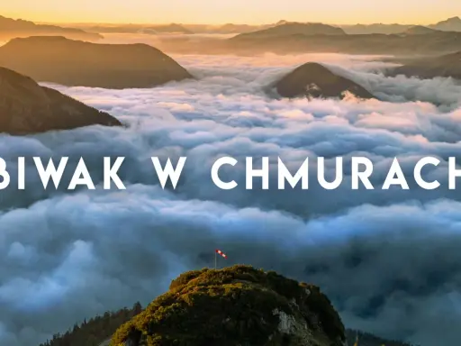 Widok z gór podczas trekkingu w Austrii. Chmury otulają szczyty, a na jednym z nich powiewa flaga.