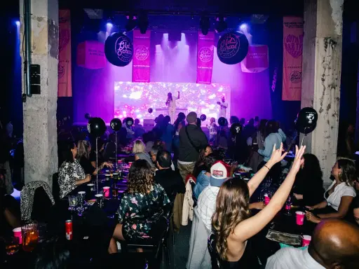Festligt event med "Old School Brunch" i Stockholm. Människor sitter vid borden, en artist uppträder på scenen under lila ljus.