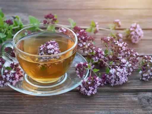 Aromatyczna herbata z oregano w szklanej filiżance, otoczona gałązkami z kwiatami. Napar ten znany jest ze swoich właściwości wspomagających trawienie i działających antybakteryjnie.