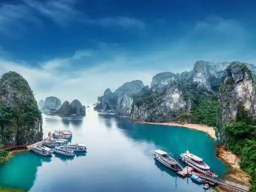 Widok na Zatokę Ha Long, kiedy do Wietnamu. Statki cumują przy turkusowej wodzie, otoczone wapiennymi wyspami porośniętymi zielenią.