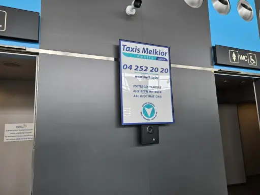 Taxi Melkior-skylt vid lgg flygplats. En övervakningskamera är monterad under skylten.
