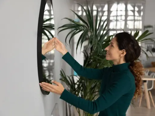 Mujer sonriente ajusta un espejo sin marco en la pared, mostrando cómo colgar un espejo sin marco para decorar su hogar.