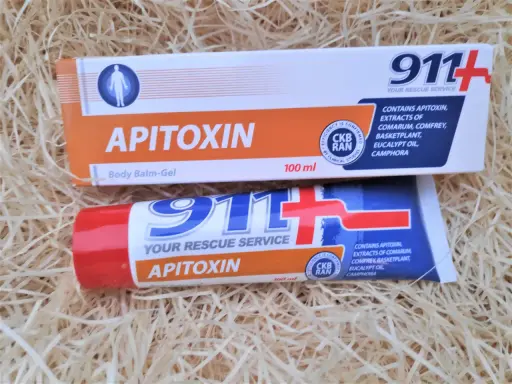 Dwa opakowania kremu z jadem pszczelim "Apitoxin" 911+ na tle słomy.